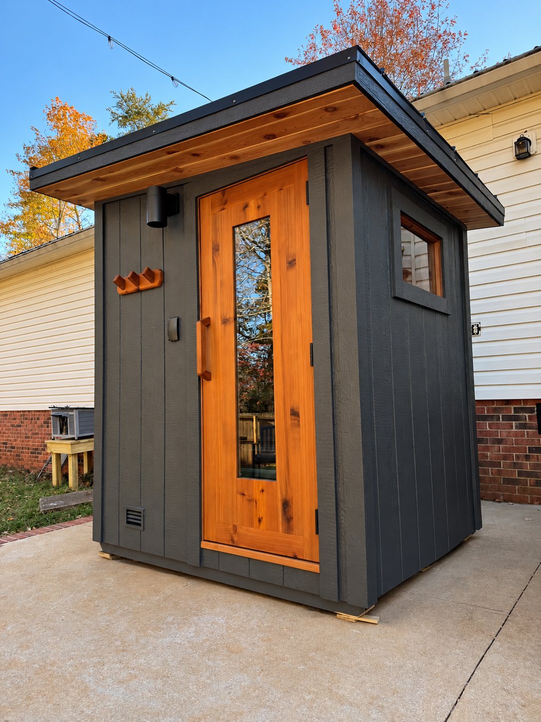 Northern Cedar sauna with dark vertical siding, a cedar door, and a sloped roof